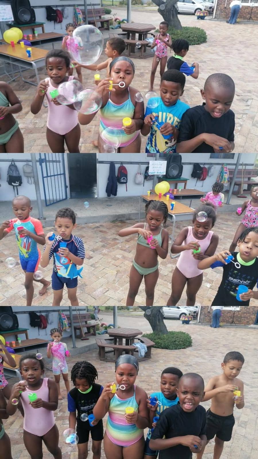 A group of children stand outdoors in swimwear, blowing bubbles and holding bubble wands at what appears to be a playground or recreational area—captured in delightful Bellville Preparatory School photos. Benches and bags are visible in the background.